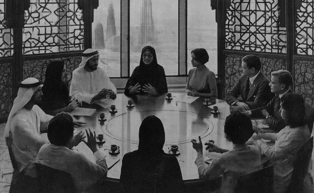 A dozen people seated around a round table with coffee cups, mid conversation, screened windows behind them.
