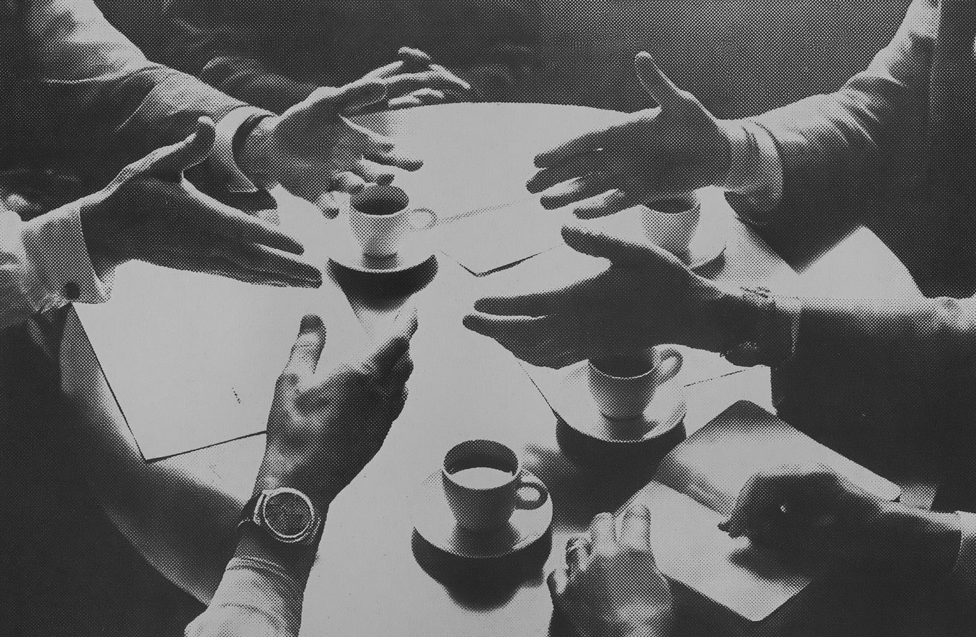 Hands reaching across a table over papers and coffee cups.